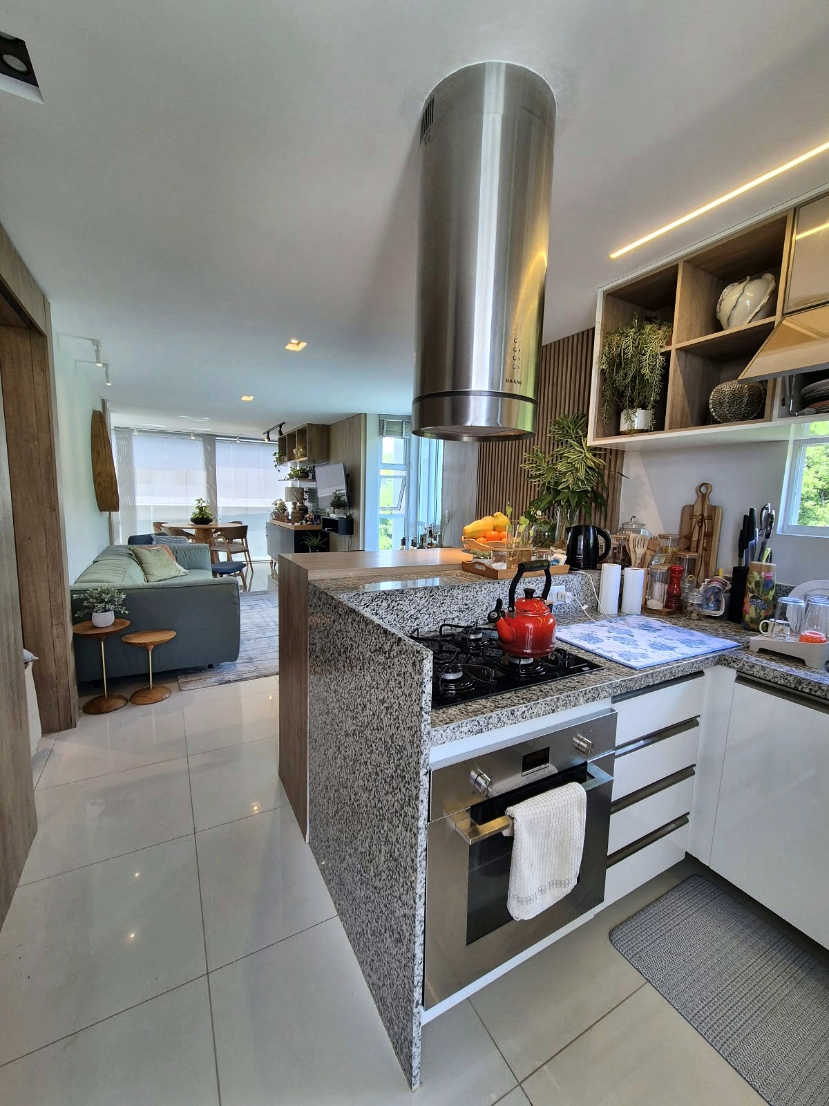 Cozinha integrada com bancada em pedra, cooktop e living ao fundo